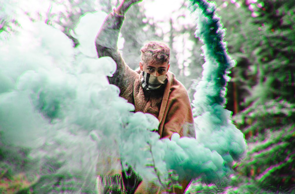 a man holding a smoke bomb with a mask on, surrounded by green smoke.