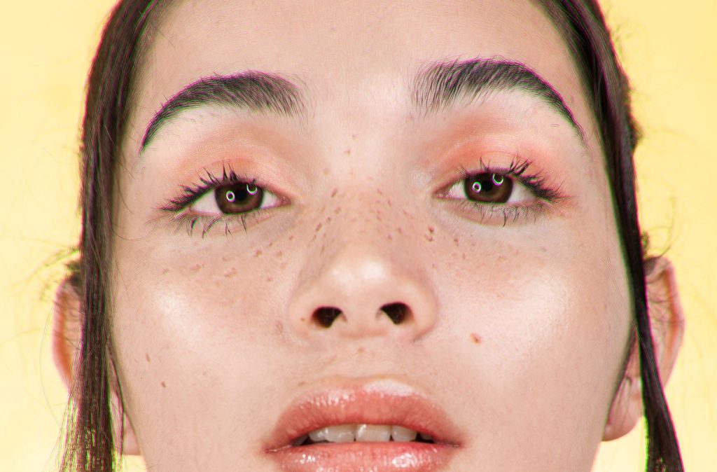 image of a white woman with pink eyeshadow on looking at the camera, with a yellow background