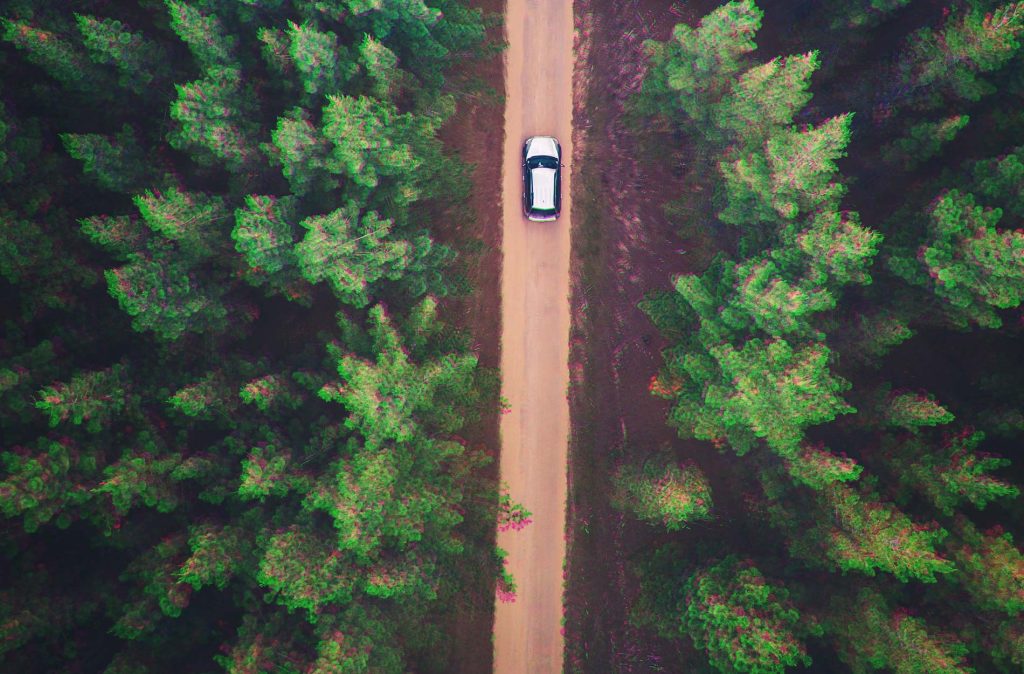 arial shot of a car going through a forest on a dirt track.